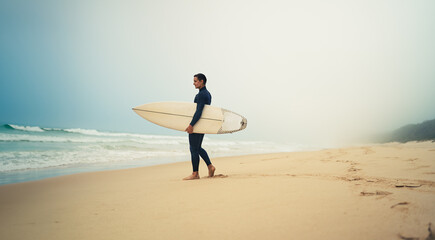 A lone surfer stands on a misty beach, holding his surfboard and looking at the waves. Serene and peaceful scene.
