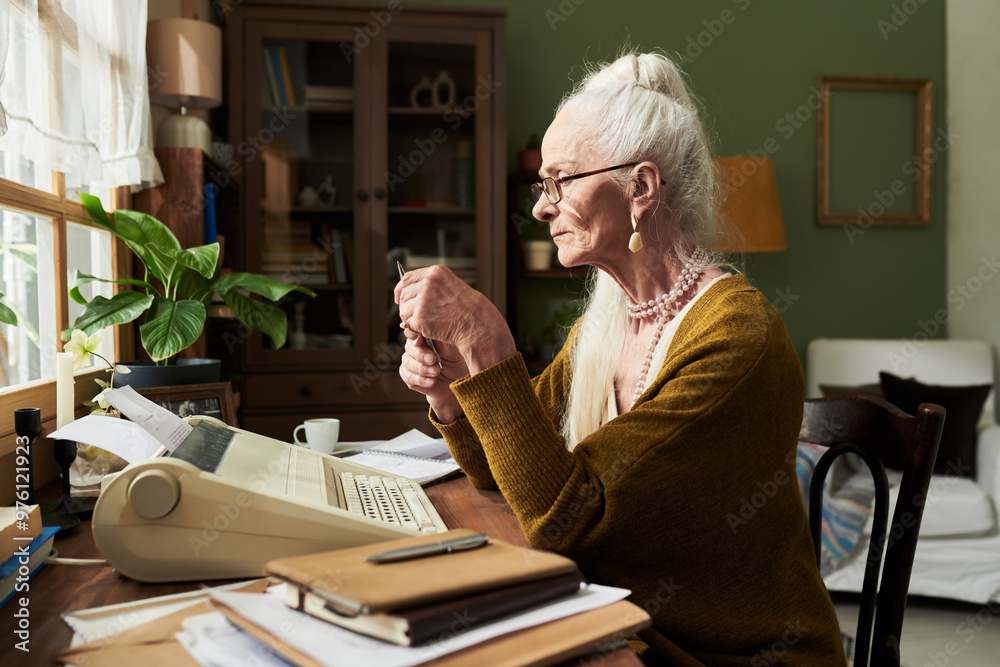 Wall mural elderly woman typing on vintage typewriter at wooden desk in cozy room filled with natural light and