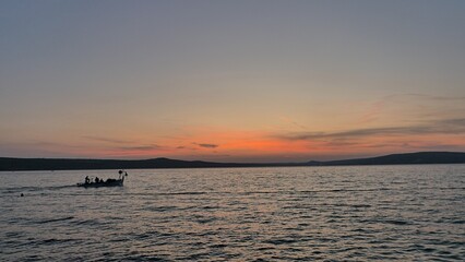 Fototapeta premium Scenery of sunset above bay near Novigrad town, northern Dalmatia, Croatia. Shoreline mountains visible in background, silhouette of fishermen boat on waves visible. 
