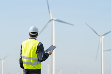 Engineer with digital tablet works on a field of wind turbines