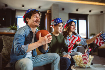 Latino family is watching rugby match with American flags.