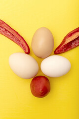 Chiken eggs, slice of a sweet bell pepper and tomato on yellow background