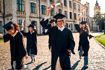 Graduates celebrating graduation. Group of students in caps and gowns rejoicing with diplomas tied...