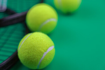 Side view close-up on a green background are two lawn tennis rackets on the left, next to them in the center are yellow tennis balls with a place for text on the side. High quality photo