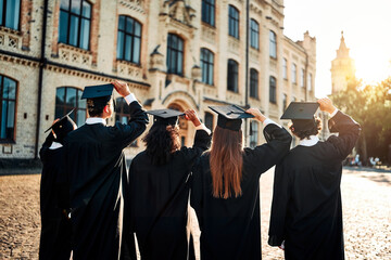 Happy students stand in front of the university and prepare to throw their academic caps up to the...