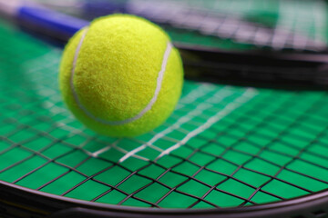 A close-up of a yellow lawn tennis ball lies against the background of rackets, behind them a green background is visible. High quality photo