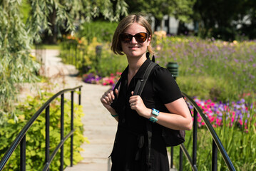 Fototapeta premium Attractive thirty year old woman with sunglasses and a black dress posing in the botanical garden during summer