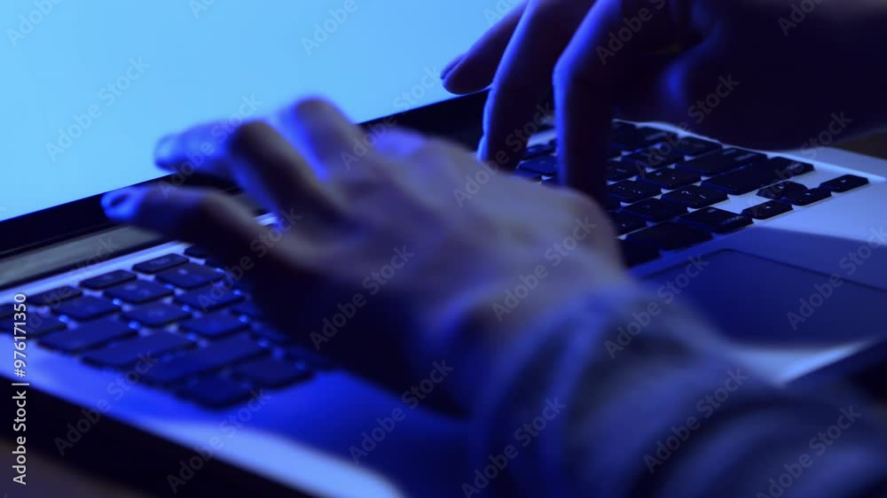 Poster a person types on a laptop keyboard, illuminated by a blue light in a dark environment, focusing int