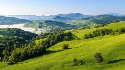 Fototapeta premium The tranquil countryside features vibrant green hills layered under the morning sun, with soft mist curling through the valley and distant mountains creating a peaceful ambiance