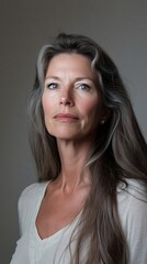 Fototapeta premium A middle-aged woman with striking features and long hair, illuminated by soft lighting on a light gray backdrop