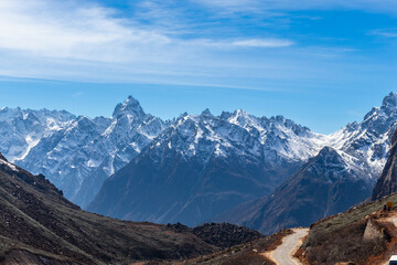 A stunning view of snow-capped mountains under a clear blue sky. Rugged peaks and a winding path create a picturesque scene, ideal for travel, adventure, nature, and outdoor themes, Sikkim, India