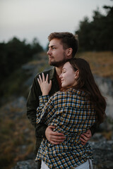 A handsome young man and a pretty woman in each other's arms are enjoying the sunset in the mountains.