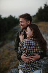 Fototapeta premium A handsome young man and a pretty woman in each other's arms are enjoying the sunset in the mountains.