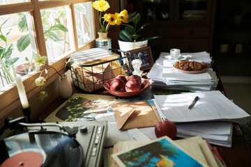 Sunlight filling cozy workspace with scattered papers, a vinyl turntable, fresh fruit, and vibrant flowers enhancing the lively atmosphere and brightening the room