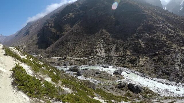 Panoramic spinning view of dirt footpath in mountain view next to Thyangmoche village and flowing Bhote Koshi river in Himalayas in Nepal in a sunny day. Snowcapped Kongde Ri mountain in background.