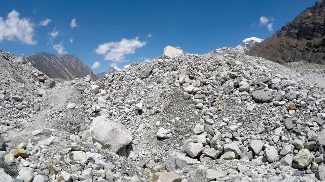 Panoramic side view of Ngozumpa glacier covered with ice and large stones and rocks in Himalayas in a sunny spring day. Chola mountain peak in the background. Real time handheld video. Extreme terrain