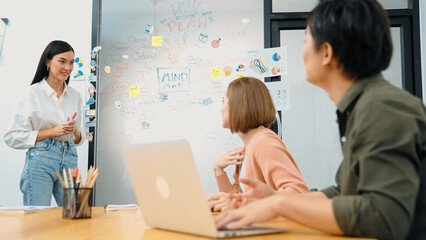 Fototapeta premium Young beautiful investor shares marketing strategy with attentive businesswoman in front of a glass board with colorful sticky notes and mind maps at creative business meeting room. Immaculate.