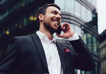 Happy man in formal wear calling to business partner for communicate during work break in financial district using 4g roaming international connection, successful male broker phoning via mobile app