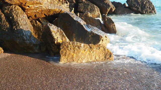 Waves with foam gently lap at rocky shore during stunning sunset over ocean. Sunlight reflects off waves as they roll onto shore, creating tranquil atmosphere at sunset by sea. Montenegro summer, Canj