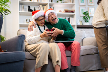 Obraz premium Asian family on Christmas Day. Everyone is happy together in a Christmas themed room filled with presents and orange lights.