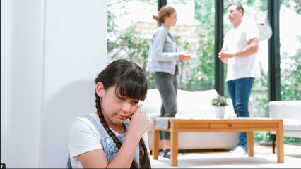 Obraz premium Stressed and unhappy young girl huddle in corner, cover her ears blocking sound of her parent arguing in background. Domestic violence at home and traumatic childhood develop to depression. Synchronos