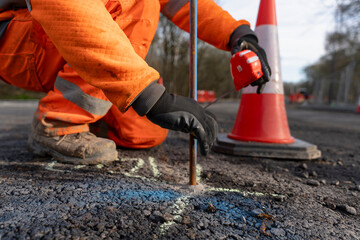 Construction Worker Marking Measurements on Road With Safety Cones Nearby During Daylight Hours
