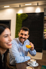 Guy listening to his friends in the cafe while drinking orange juice.