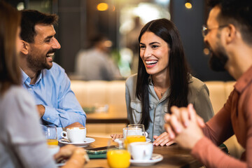 Group of friends hanging out at the cafe. The girl takes the lead in the conversation. Drinking orange juice and coffee.
