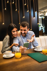 Couple went on a date in a restaurant. They are looking at the phone. They drink coffee and orange juice.