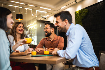 Group of friends sitting at cafe and drinking orange juice.