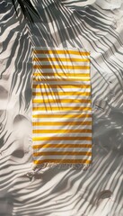 Vibrant yellow and white striped beach towel spread out on a sandy beach, with palm leaf shadows