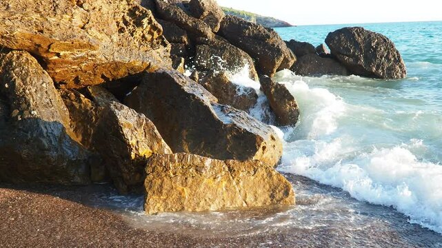 Waves with foam gently lap at rocky shore during stunning sunset over ocean. Sunlight reflects off waves as they roll onto shore, creating tranquil atmosphere at sunset by sea. Montenegro summer, Canj