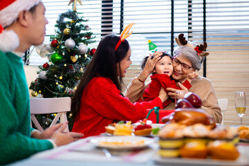 Asian family on Christmas Day. Everyone is happy together in a Christmas themed room filled with presents and orange lights.