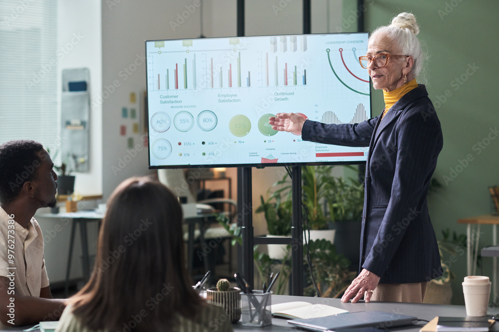 Poster senior businesswoman presenting data analysis on large screen to diverse team in modern office meeti