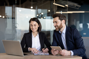 Two business professionals engaged in collaborative work using digital technology. Smiling colleagues working on project with laptop and tablet, promoting teamwork, business strategy, connection.