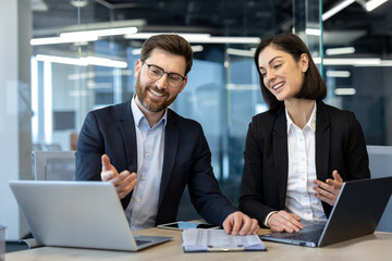 Business professionals engaged in a collaborative discussion using laptops at modern office. Two...