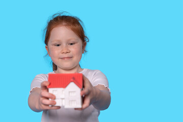 Happy Girl Proudly Displays Her Small House Model Against  Vibrant Blue Background