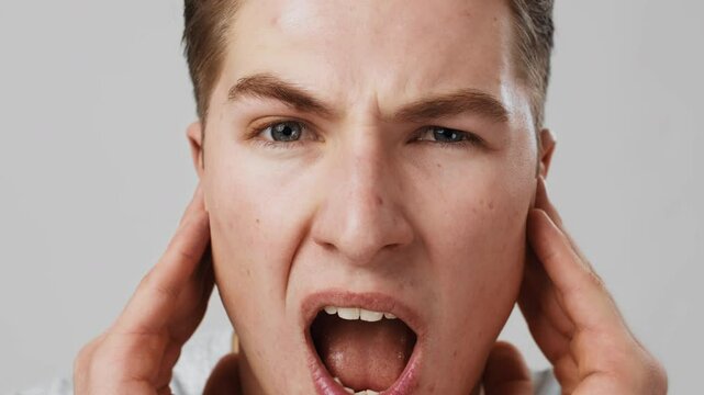 Increased hearing sensitivity. Close up portrait of young man suffering from noise, rubbing ears, slow motion