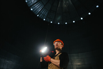 Male worker in safety helmet with flashlight in hands inside storage tank. Inside the grain silo. © dsheremeta