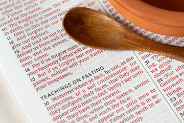 Teaching on fasting verses in holy bible book with empty dish and wooden spoon. Close-up. Christian biblical concept of spiritual food and humility.