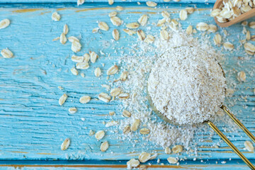 Oat flour ingredient in measuring cup placed on wooden table with oatmeal flakes. Top view. Gluten-free baking concept.