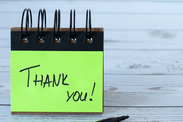 Thank you, handwritten quote on green paper note placed on wooden desk. Close-up. The concept of...