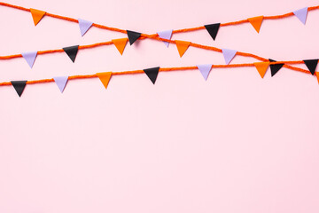 Halloween garland made of paper flags on pastel pink background.