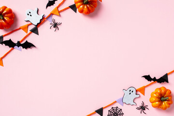 Happy Halloween holiday concept. Flat lay composition with paper garland, pumpkins, bats, ghosts, spiders on pastel pink background. Top view with copy space