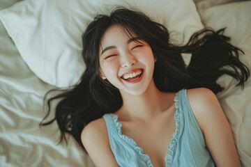 Fototapeta premium Beautiful Korean women, in a happy mood, wearing a blue dress, smiling and laughing, with a white pillow in the background, laying on a bed, in natural light, captured with a Canon EOS