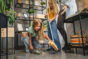 Daughters clean broken vase with a broom and dustpan in living room