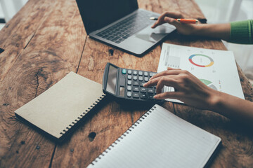 Financial Focus:  A woman's hands meticulously calculate expenses, surrounded by a laptop, charts,...