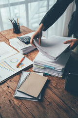 Businesswoman at Desk: Hands reach for a stack of paperwork amidst a cluttered desk, showcasing the...