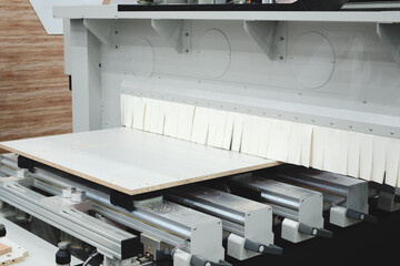 A woodworking shop with a large machine cutting a piece of wood. The machine is surrounded by a lot...