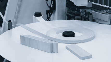 A machine is cutting a strip of wood. The machine is surrounded by other machines